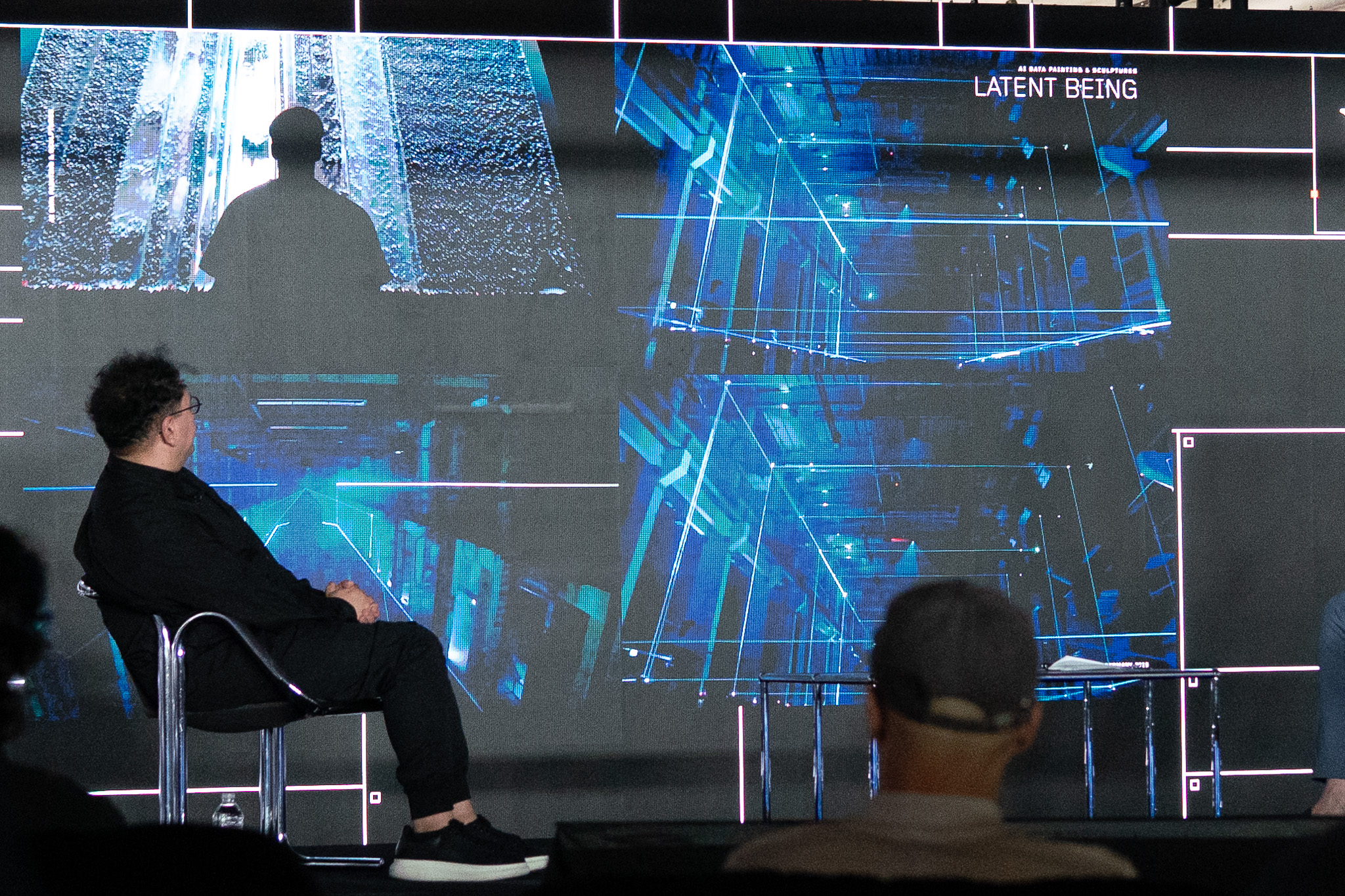 Refik Anadol watching his work Latent Being unfold across the stage wall in blues and greens