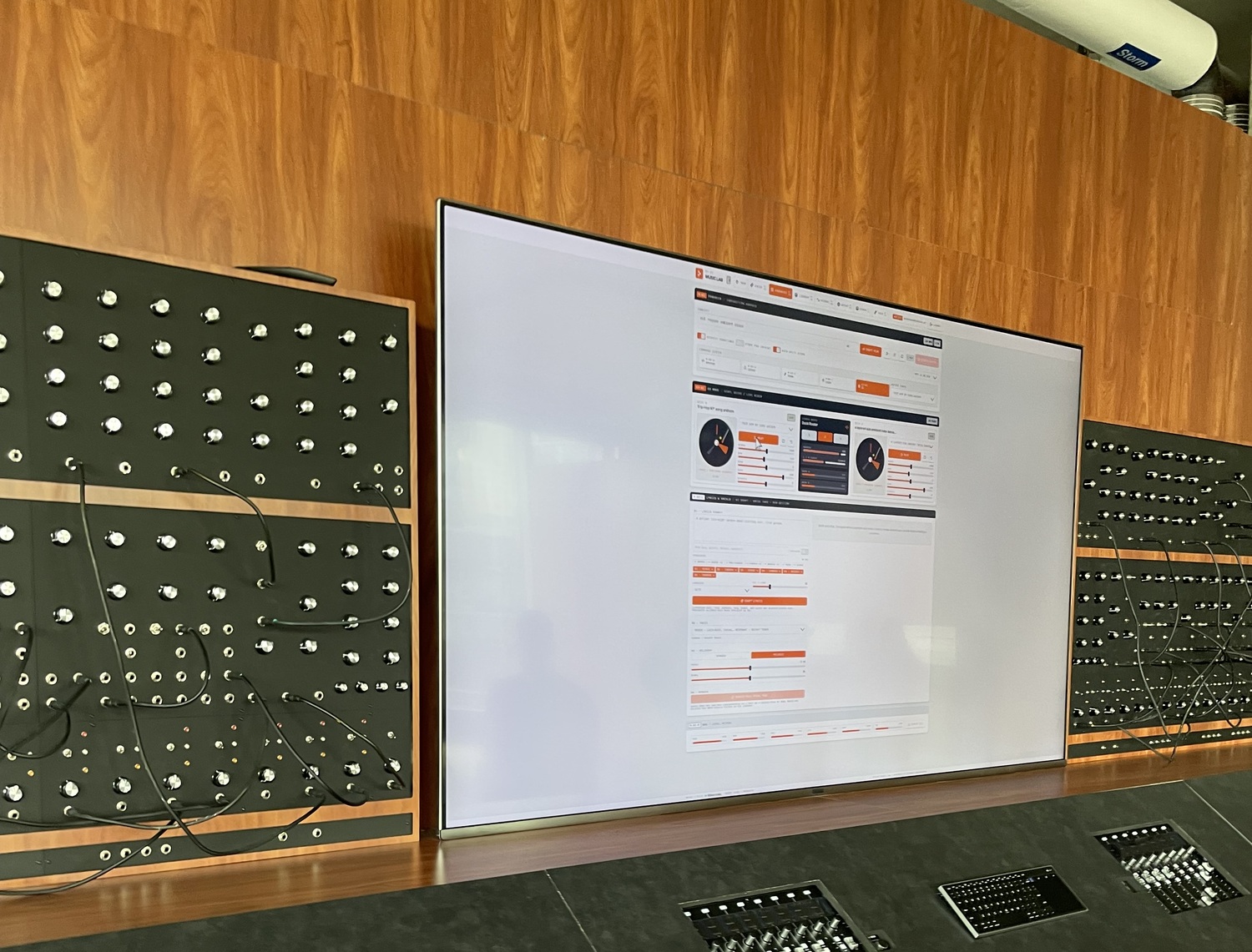 The MUSICLAB software interface on a large screen, flanked by patch panels and embedded mixing consoles