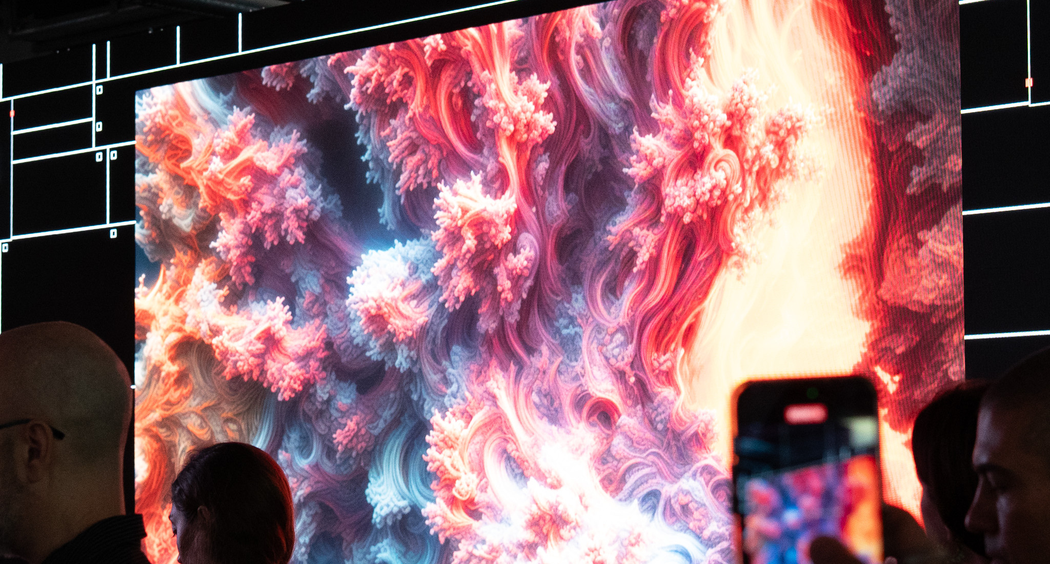 A vast coral-like fractal in pinks and blues filling the big LED wall, a visitor filming it on a phone